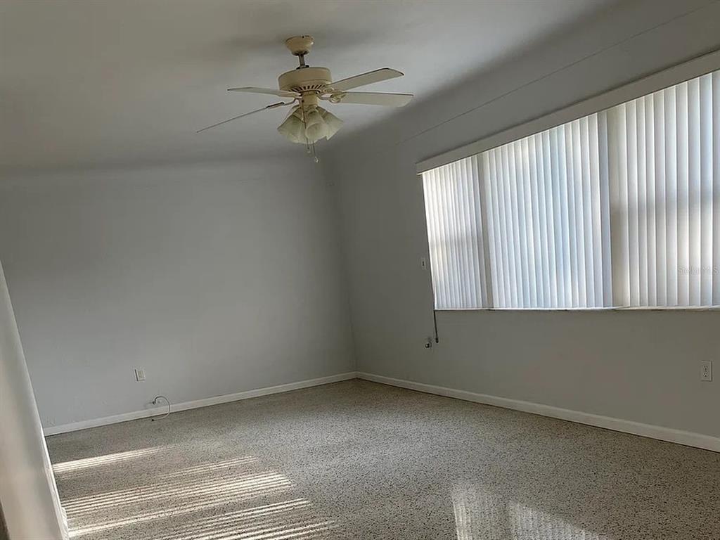 An empty room features light-colored walls, speckled carpeting, a ceiling fan, and vertical window blinds — 5003 58TH WAY N, KENNETH CITY, FL