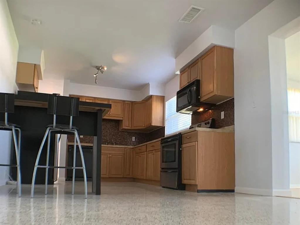 A kitchen with light wood cabinets, a dark island, and a tiled backsplash — 5003 58TH WAY N, KENNETH CITY, FL