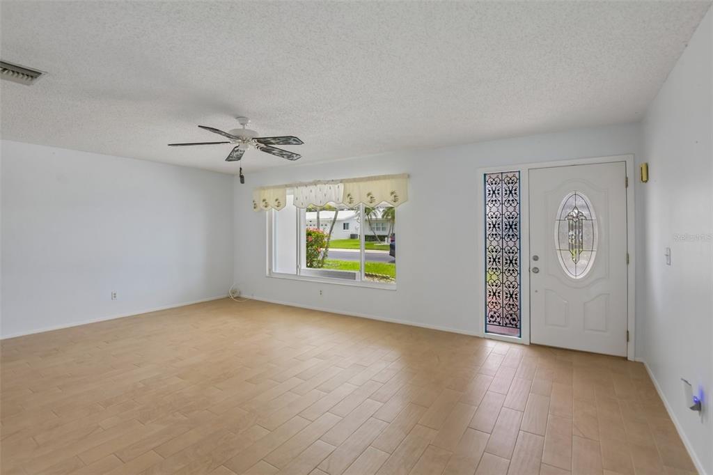 An empty living room features light wood-look tile flooring, a ceiling fan, and a front door — 3549 98TH AVENUE N, PINELLAS PARK, FL