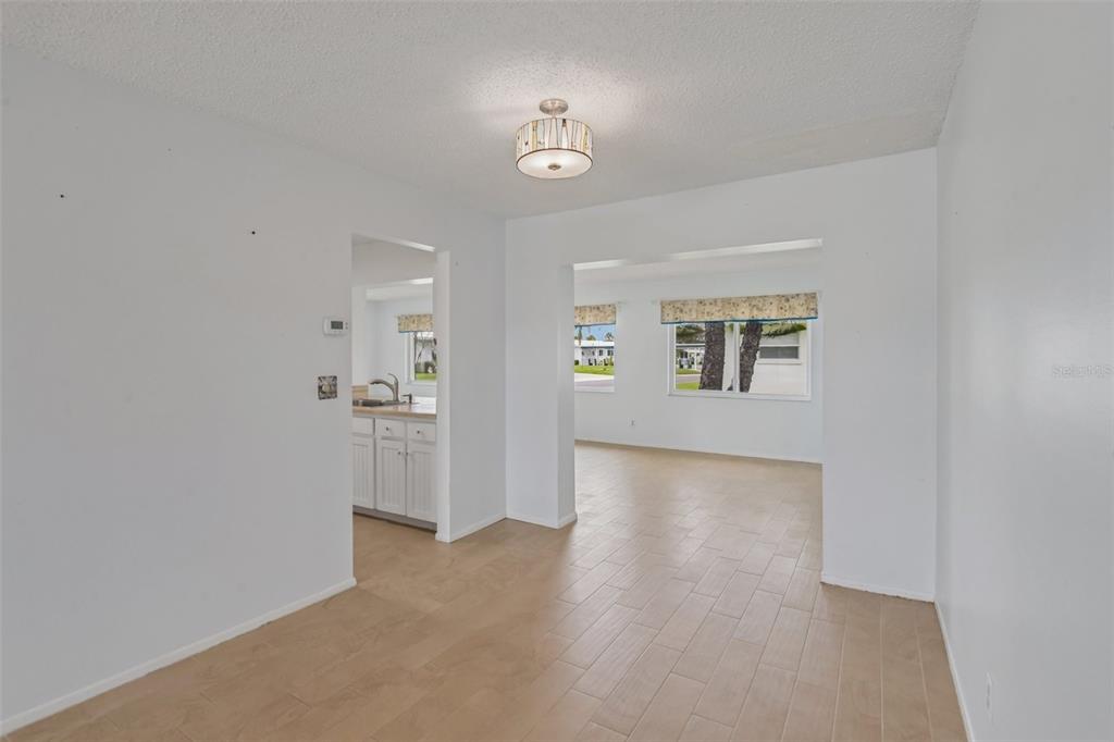 A dining area with light wood-look tile flooring connects to a kitchen and living room — 3549 98TH AVENUE N, PINELLAS PARK, FL