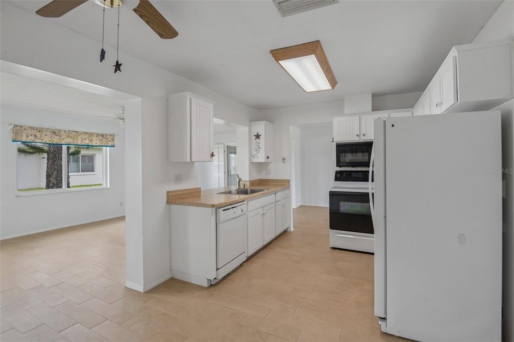 A kitchen with white cabinets, wood-look countertops, and white appliances features light-colored tile flooring — 3549 98TH AVENUE N, PINELLAS PARK, FL