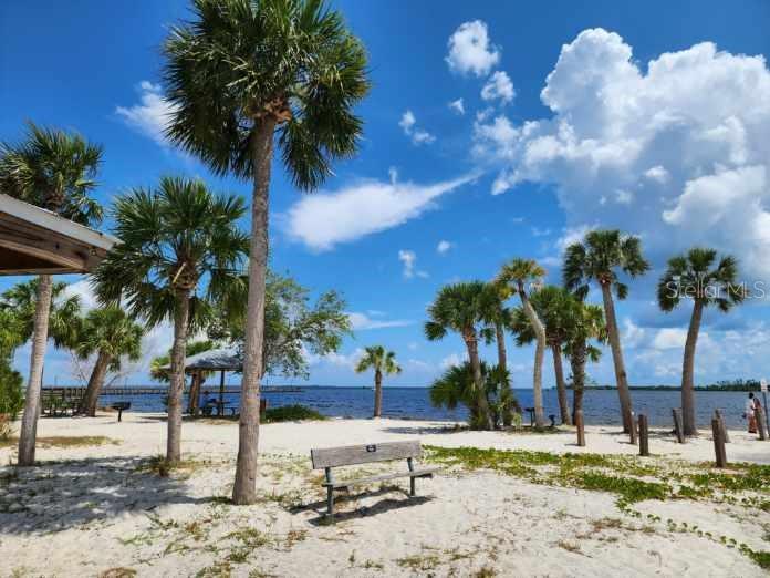 A sandy beach area features palm trees, a wooden bench, and a view of the water — 3135 CABARET STREET, PORT CHARLOTTE, FL