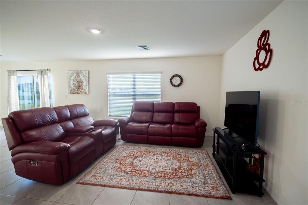 A living room features two red leather sofas, a patterned area rug, and a television — 16546 MOSAIC OAR DRIVE, WIMAUMA, FL