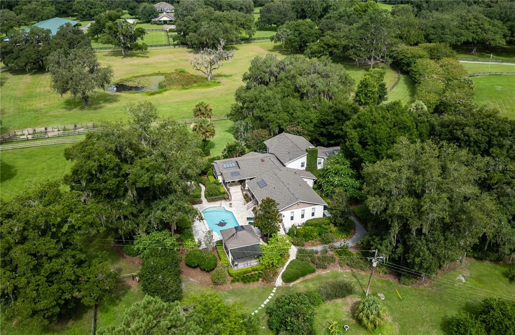 An aerial view shows a house with a swimming pool surrounded by trees and pastures — 12500 NW 100TH STREET, OCALA, FL