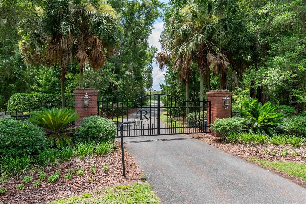 A paved driveway leads to a gated entrance flanked by brick pillars and palm trees — 12500 NW 100TH STREET, OCALA, FL