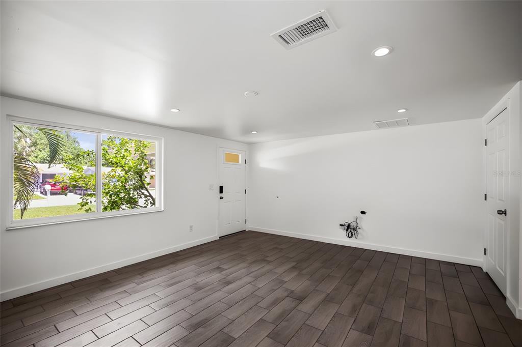 An empty room features white walls, dark wood-look tile flooring, a window, and a door — 5646 QUIST DRIVE, PORT RICHEY, FL