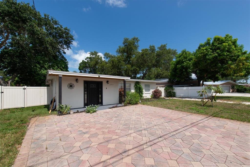 A single-story house with a paved driveway and white fence under a clear blue sky — 12812 LAKE DRIVE, LARGO, FL