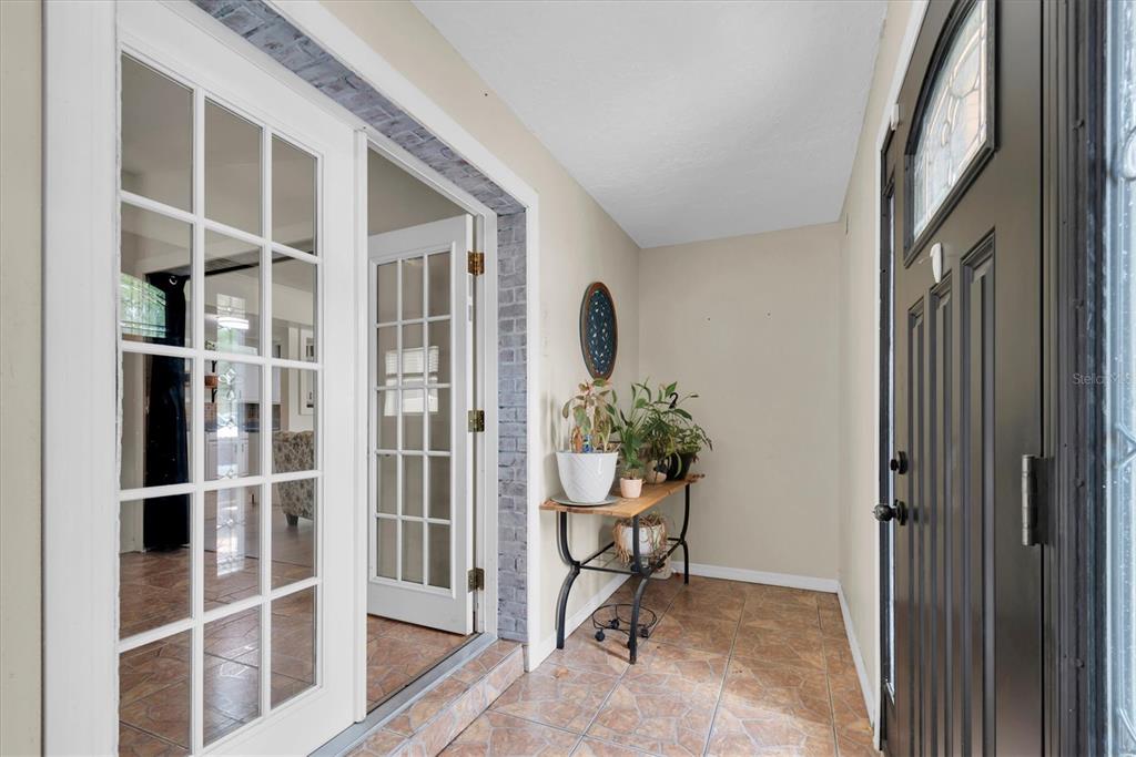 A tiled entryway features a black front door, a glass French door, and a console table — 12812 LAKE DRIVE, LARGO, FL