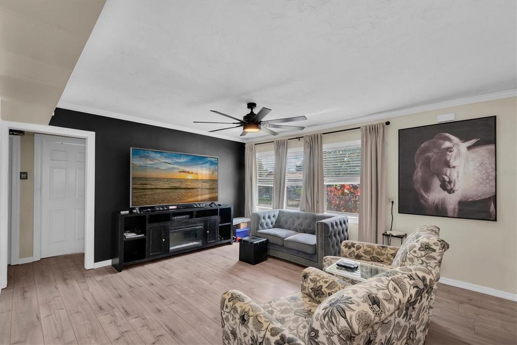 A living room features a black accent wall with a television, gray sofa, and patterned armchair — 12812 LAKE DRIVE, LARGO, FL