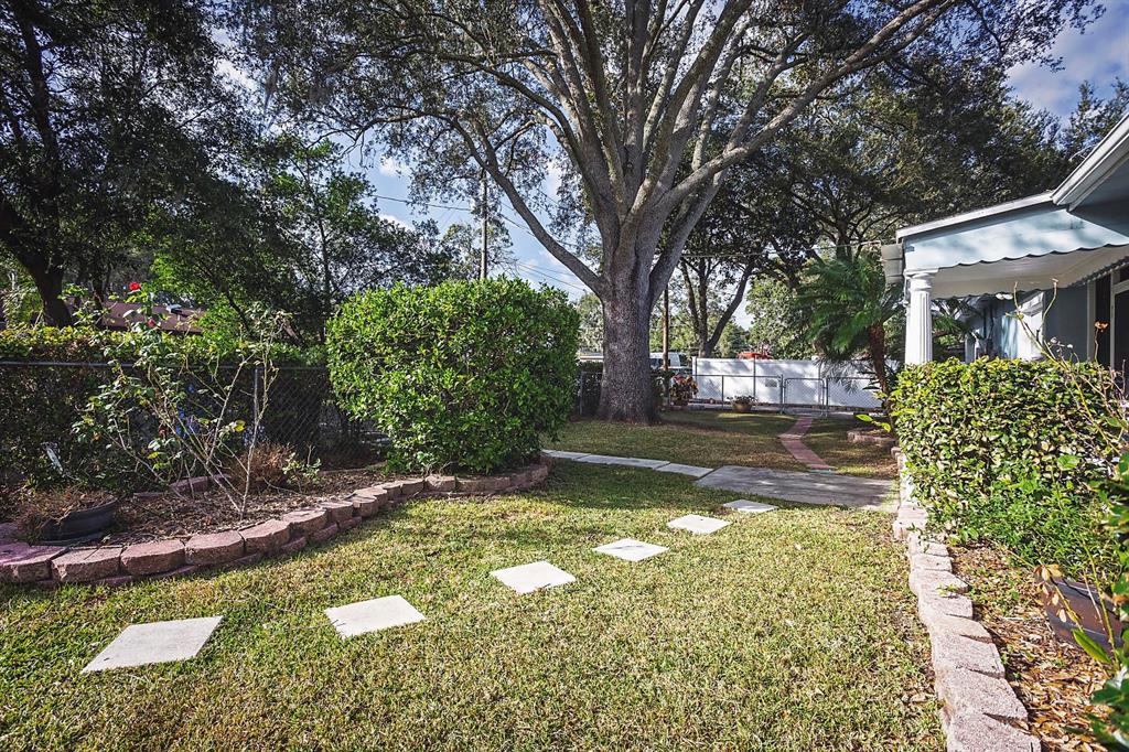 A grassy yard features a stone path, a large tree, and a brick-edged garden bed — 2614 FAIRVIEW AVENUE, SEFFNER, FL
