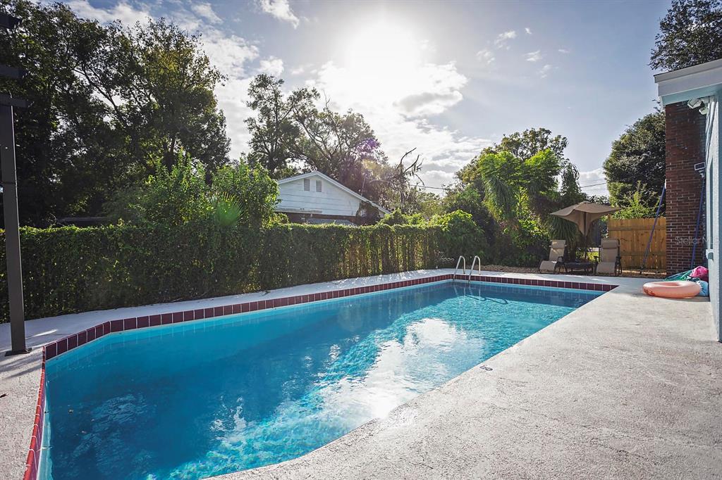 A rectangular swimming pool with red tile coping sits in a backyard with landscaping — 2614 FAIRVIEW AVENUE, SEFFNER, FL