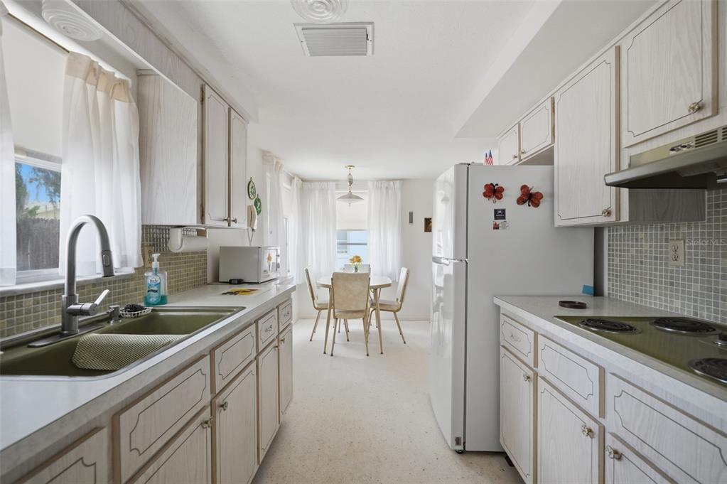 A galley kitchen with white cabinets, a green sink, and an adjacent dining area — 1207 LODESTAR DRIVE, HOLIDAY, FL