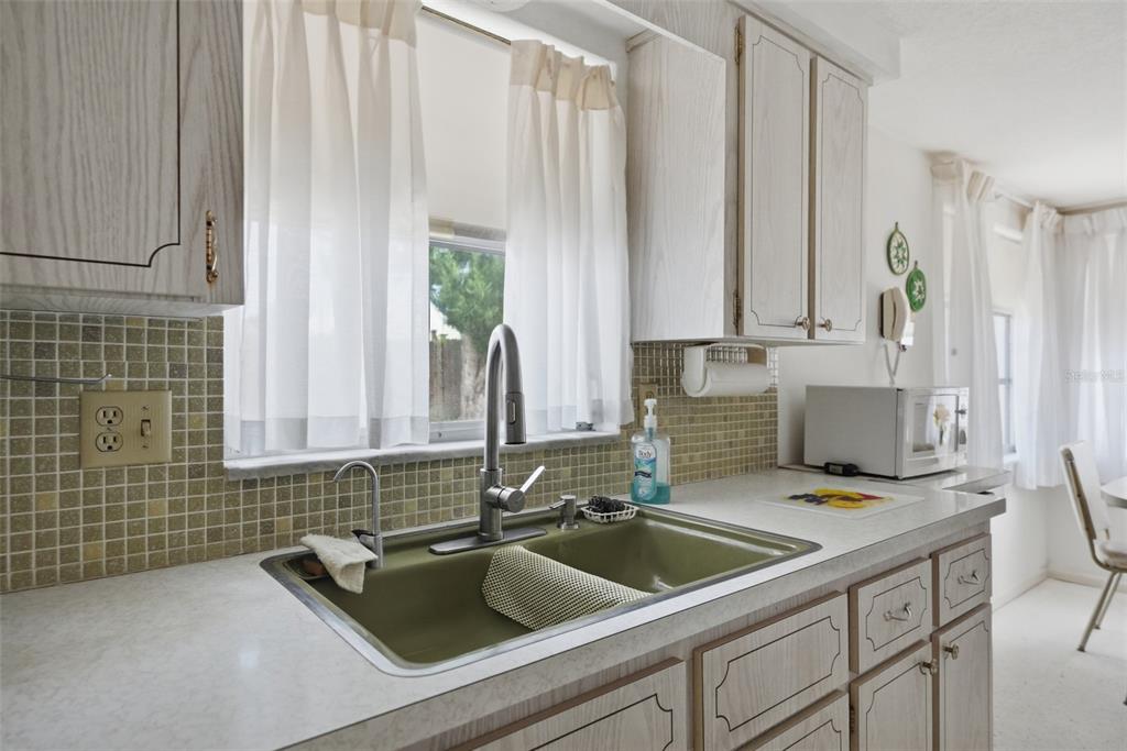 A kitchen features a green double-basin sink, light wood cabinets, and a tiled backsplash — 1207 LODESTAR DRIVE, HOLIDAY, FL