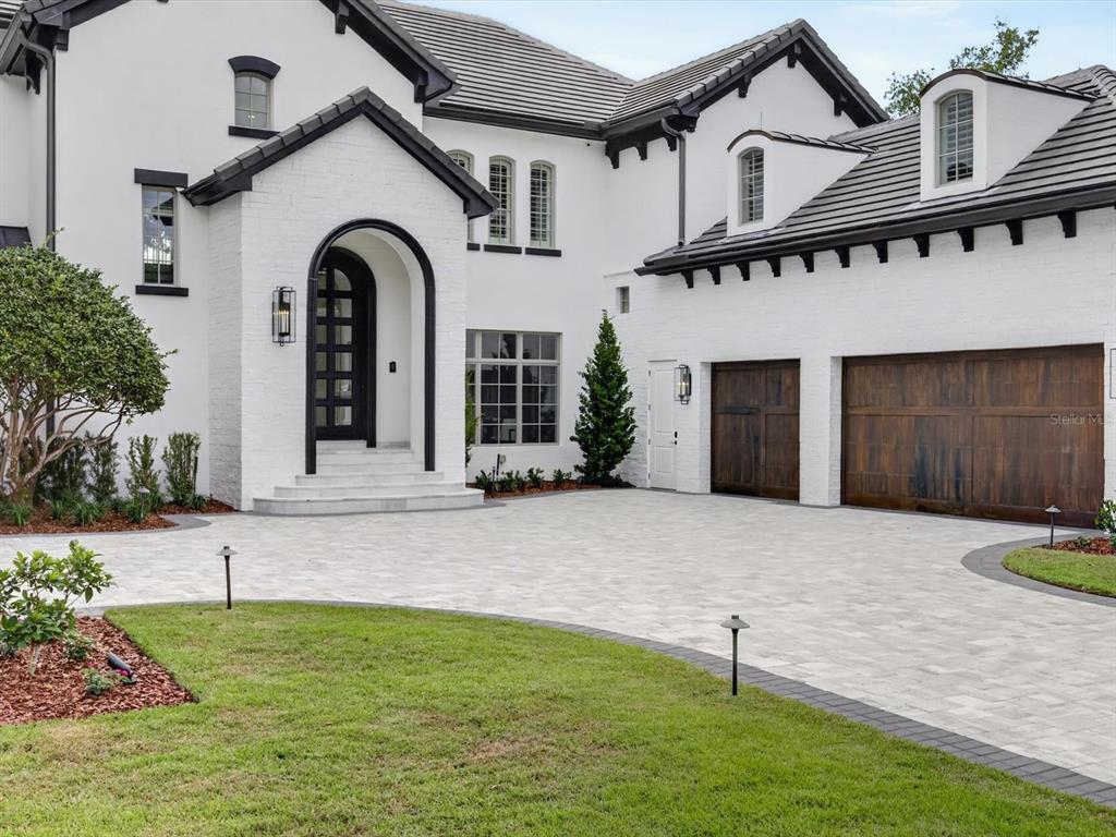 A white brick house with a dark roof, arched front door, and two wooden garage doors — 9832 LAUREL VALLEY DRIVE, WINDERMERE, FL