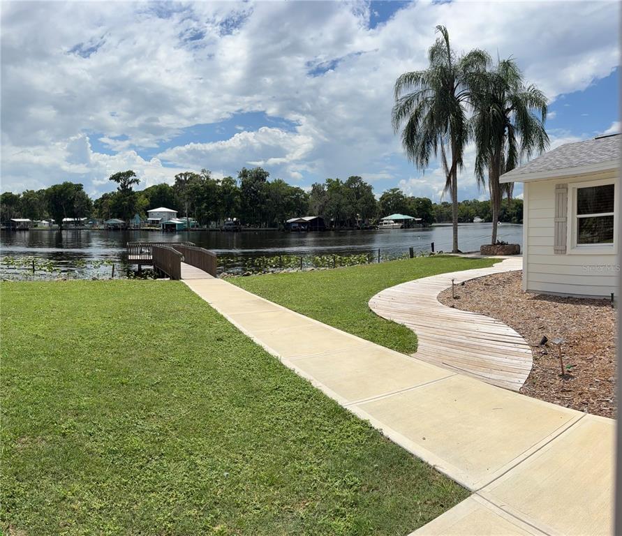 An aerial view shows a waterfront house with a lawn, palm trees, and a wooden dock — 1645 SPRING GARDEN DRIVE, ASTOR, FL