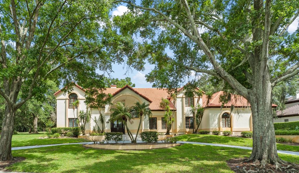 A two-story stucco house with a red tile roof sits behind large oak trees — 5073 LATROBE DR, WINDERMERE, FL