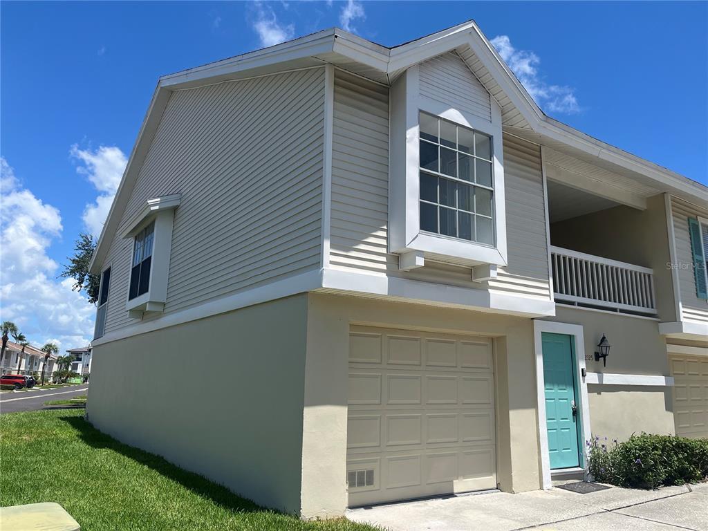 A two-story townhouse exterior with beige siding, a garage, and a light blue front door — 12325 SUN VISTA COURT W, TREASURE ISLAND, FL