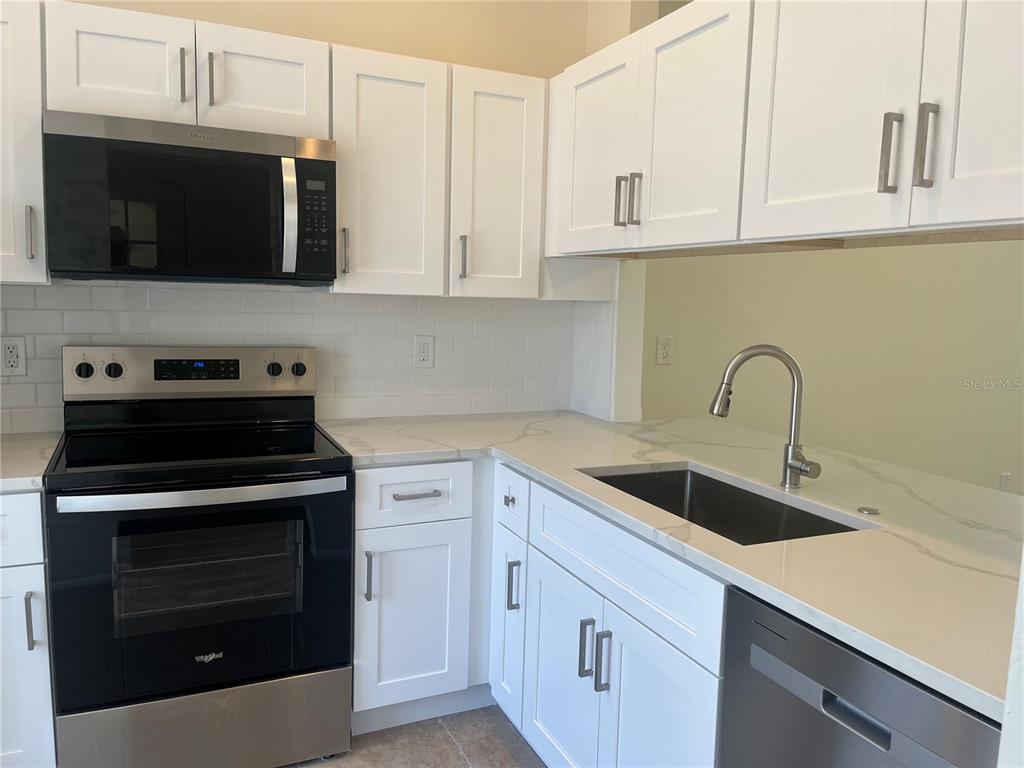 A kitchen features white cabinets, stainless steel appliances, and light-colored countertops with a subway tile backsplash — 12325 SUN VISTA COURT W, TREASURE ISLAND, FL