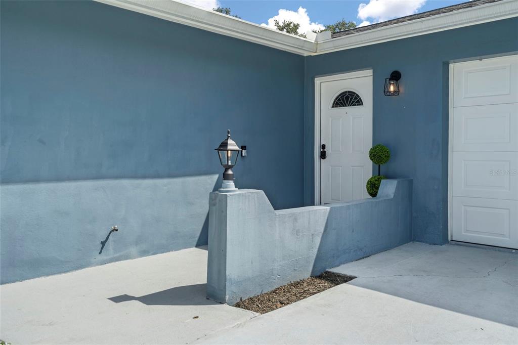 A blue exterior wall features a white door, a low concrete wall, and a lamp — 6917 DUNNETT AVENUE N, ST PETERSBURG, FL