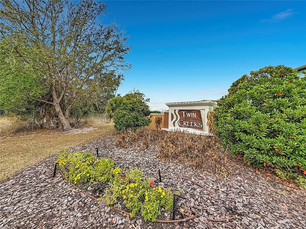 A sign for Twin Creeks stands in a landscaped garden bed with mulch and shrubs — 12728 LEMON PEPPER DRIVE, RIVERVIEW, FL