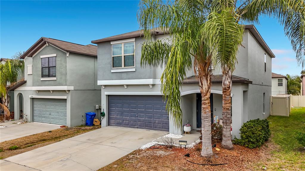 A two-story suburban house with a gray stucco exterior, a two-car garage, and palm trees — 12728 LEMON PEPPER DRIVE, RIVERVIEW, FL