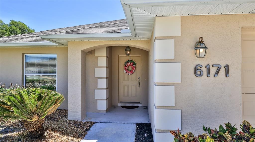 The exterior of a beige house features a covered entryway with a decorative front door — 6171 SABAL POINT CIRCLE, PORT ORANGE, FL