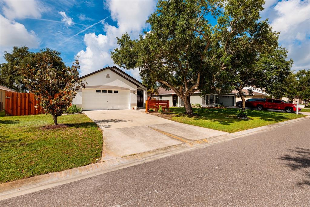 A single-story house with a white garage, a concrete driveway, and large trees in front — 4909 70TH STREET E, PALMETTO, FL