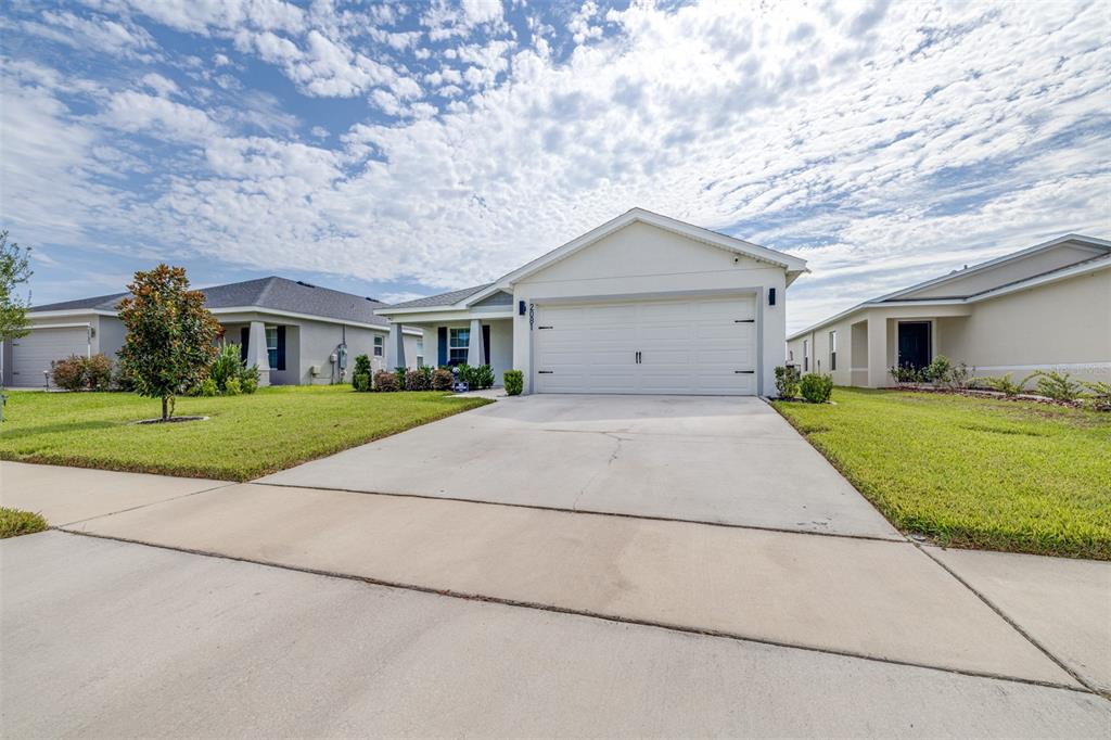 A single-story suburban house with a white garage, concrete driveway, and green lawn — 2081 GOLDEN BEAK DRIVE, EAGLE LAKE, FL
