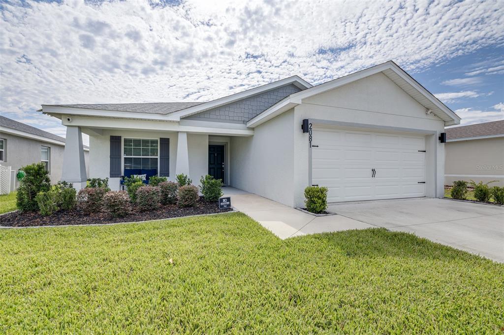 A single-story house with a white stucco exterior, a two-car garage, and a landscaped front yard — 2081 GOLDEN BEAK DRIVE, EAGLE LAKE, FL