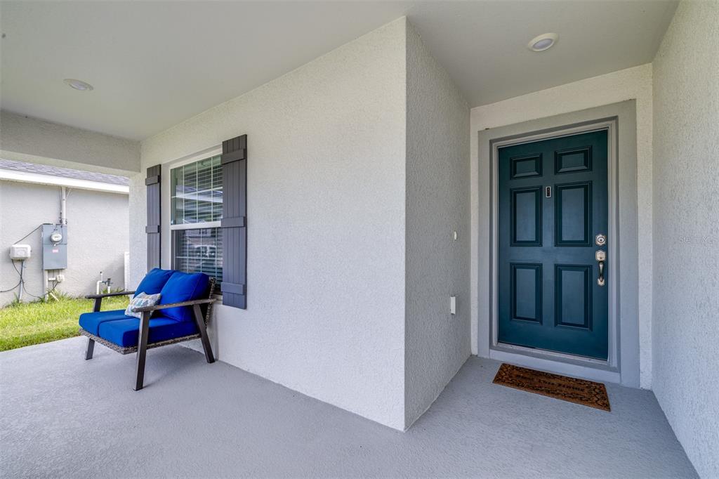 A covered front porch features a blue chair, a dark teal door, and gray flooring — 2081 GOLDEN BEAK DRIVE, EAGLE LAKE, FL