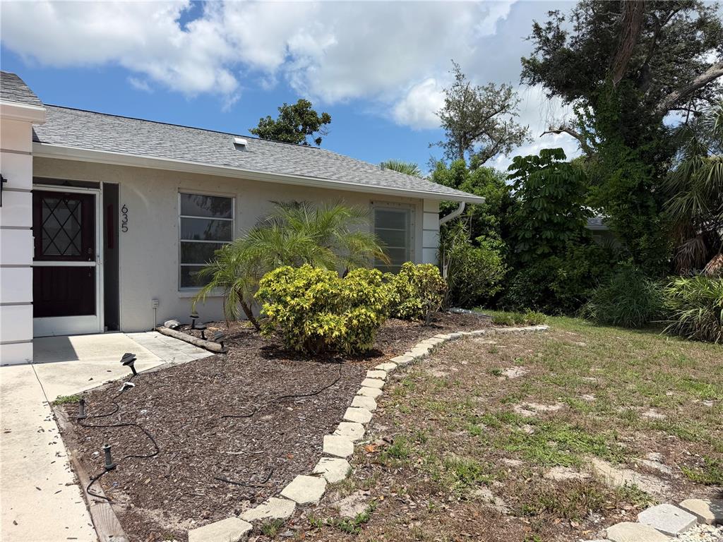 A single-story house exterior features a light-colored facade, a gray shingled roof, and landscaping — 635 HARVEY STREET, ENGLEWOOD, FL