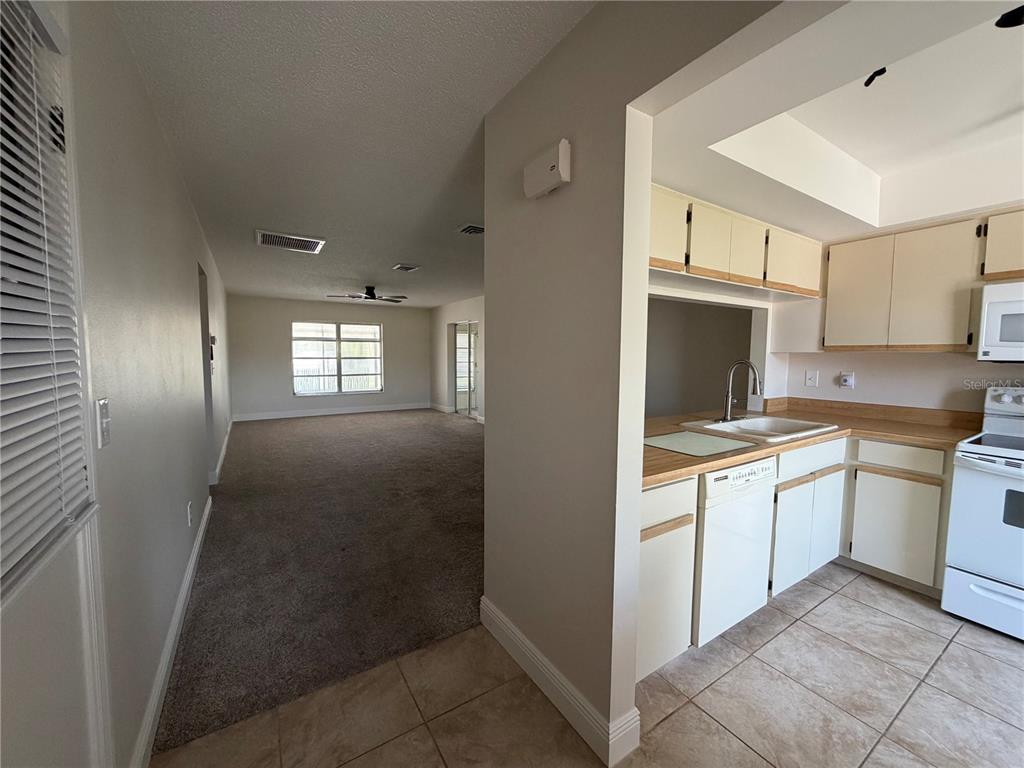 A kitchen with white cabinets and tile flooring overlooks a carpeted living area — 635 HARVEY STREET, ENGLEWOOD, FL