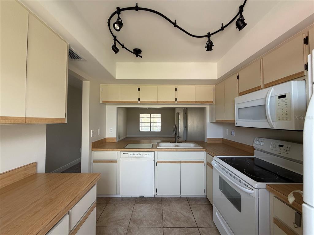A kitchen features light-colored cabinets, laminate countertops, white appliances, and a track lighting fixture — 635 HARVEY STREET, ENGLEWOOD, FL