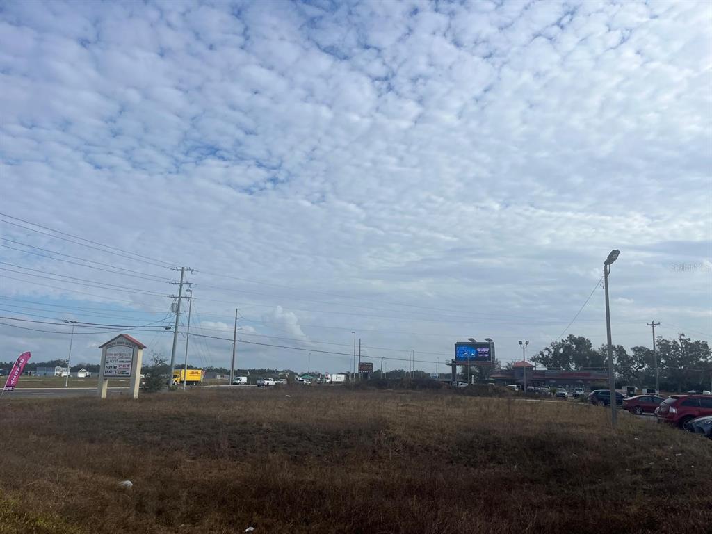 A vacant, grassy lot sits beside a commercial shopping center under a cloudy sky — 2401 GRIFFIN ROAD UNIT E, BARTOW, FL