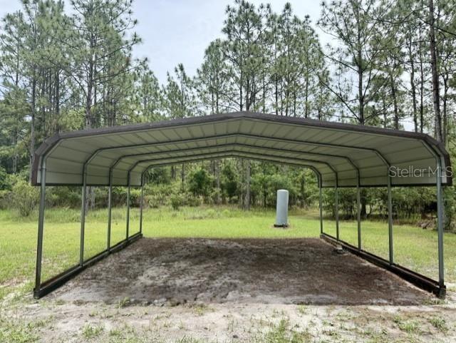 A metal carport stands on a dirt pad in a grassy, wooded outdoor area — 4890 NW 55TH AVENUE, BELL, FL
