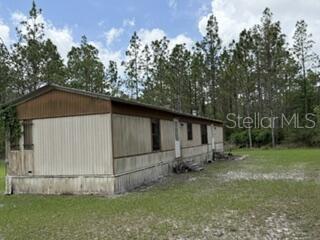 A single-story mobile home sits on a grassy lot bordered by a dense pine forest — 4890 NW 55TH AVENUE, BELL, FL