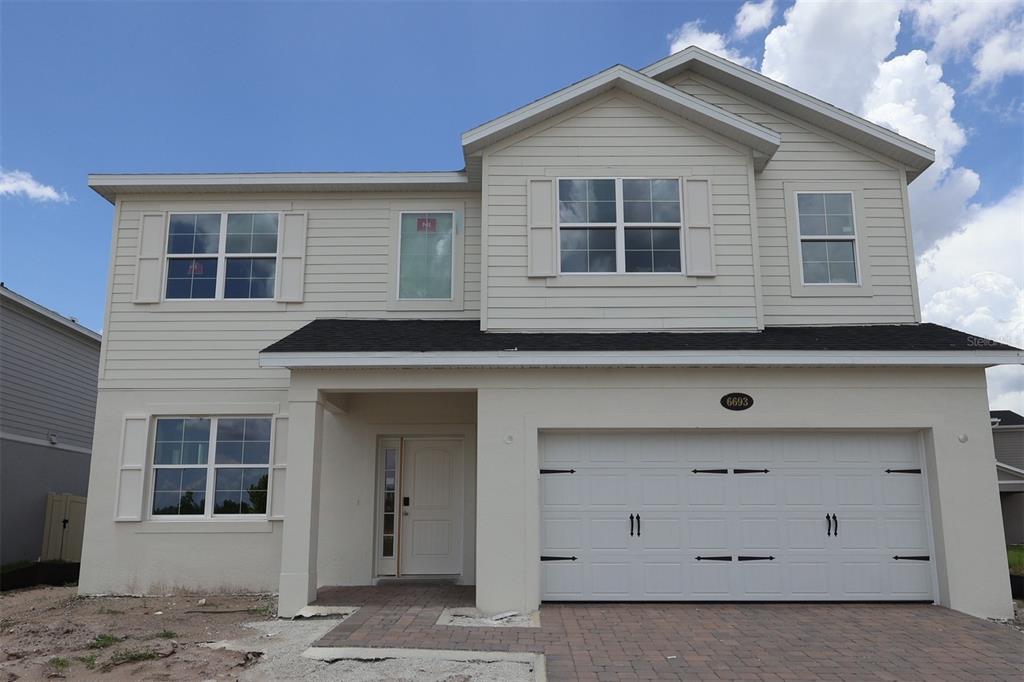 A two-story suburban house with light siding, a white garage, and a paved driveway — 6693 YELLOW WARBLER BEND, ST CLOUD, FL