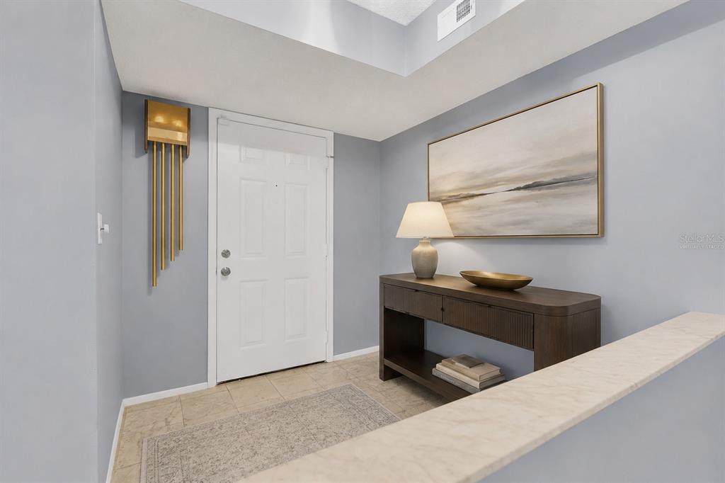 An entryway features a white door, a console table with a lamp, and wall art — 8198 TERRACE GARDEN DRIVE UNIT 511, ST PETERSBURG, FL