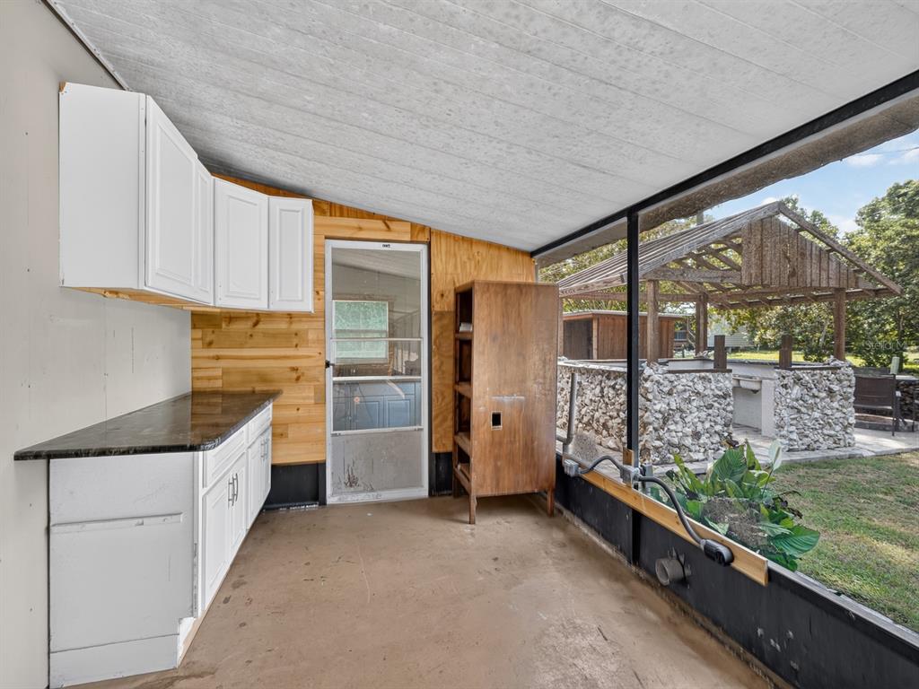 A screened-in porch features white cabinets, a dark countertop, wood paneling, and an outdoor structure — 25101 NE 131ST PLACE, FORT MC COY, FL