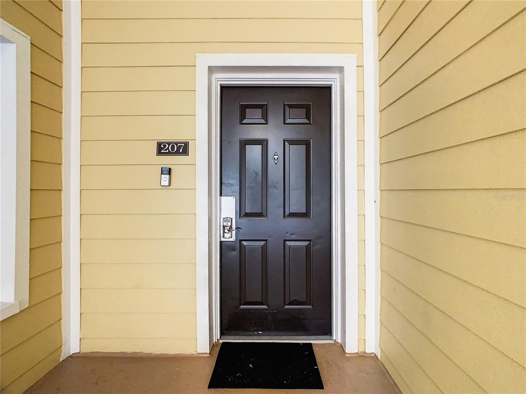 A dark brown front door with a keypad lock is set in a yellow-sided exterior wall — 3050 PIRATES RETREAT COURT UNIT 207, KISSIMMEE, FL