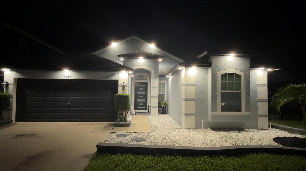 A single-story house with a dark garage door, light-colored stucco, and white rock landscaping — 4037 WARWICK HILLS DRIVE, WESLEY CHAPEL, FL