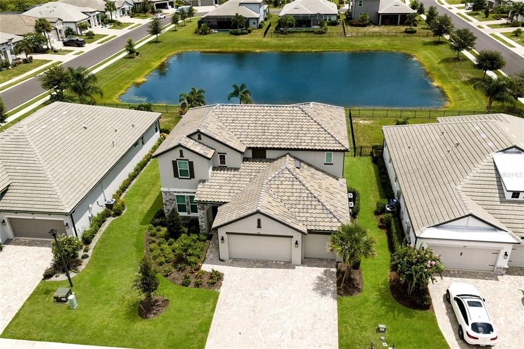An aerial view shows a two-story house with a tiled roof next to a pond — 4811 HONEY DEW LANE, BRADENTON, FL