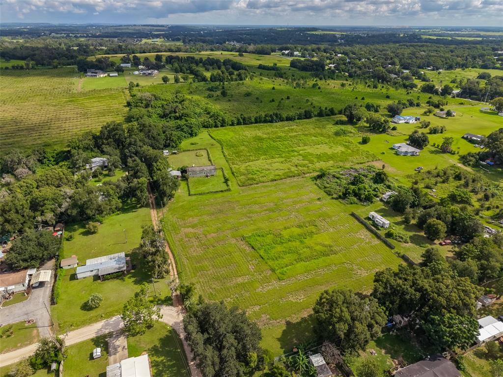 An aerial view shows a rural property with a house, open fields, and surrounding trees — 7408 HYLAN STREET, ZEPHYRHILLS, FL