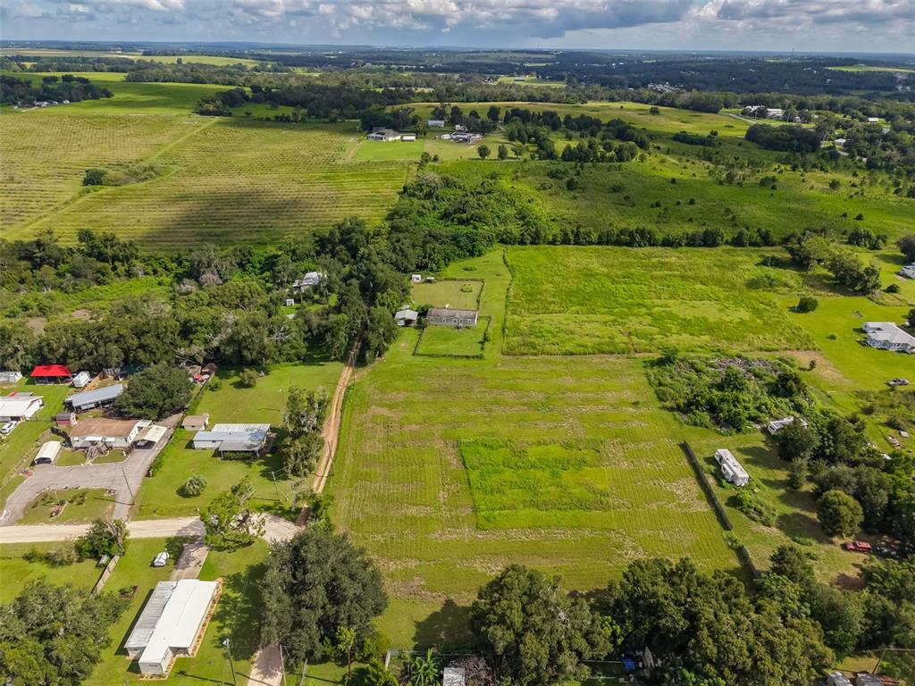 An aerial view shows a rural property with a house, outbuildings, and surrounding grassy fields — 7408 HYLAN STREET, ZEPHYRHILLS, FL