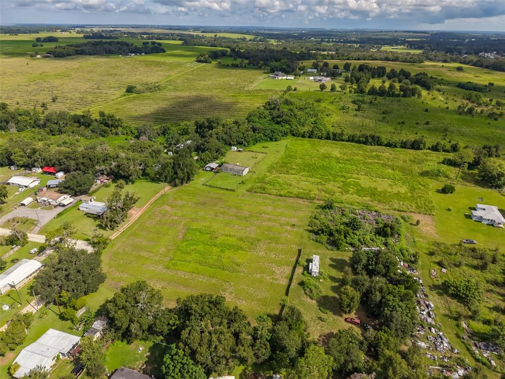 An aerial view shows a rural property with multiple houses, open fields, and scattered trees — 7408 HYLAN STREET, ZEPHYRHILLS, FL