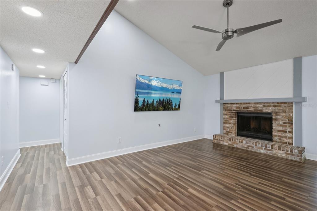 A living room features a vaulted ceiling, wood-look flooring, a brick fireplace, and a wall-mounted television — 3613 COPPERTREE CIRCLE, BRANDON, FL