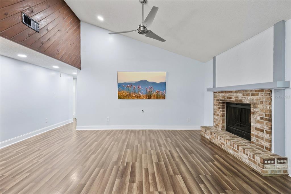 A living room features a vaulted ceiling, wood-look flooring, a brick fireplace, and wood paneling — 3613 COPPERTREE CIRCLE, BRANDON, FL