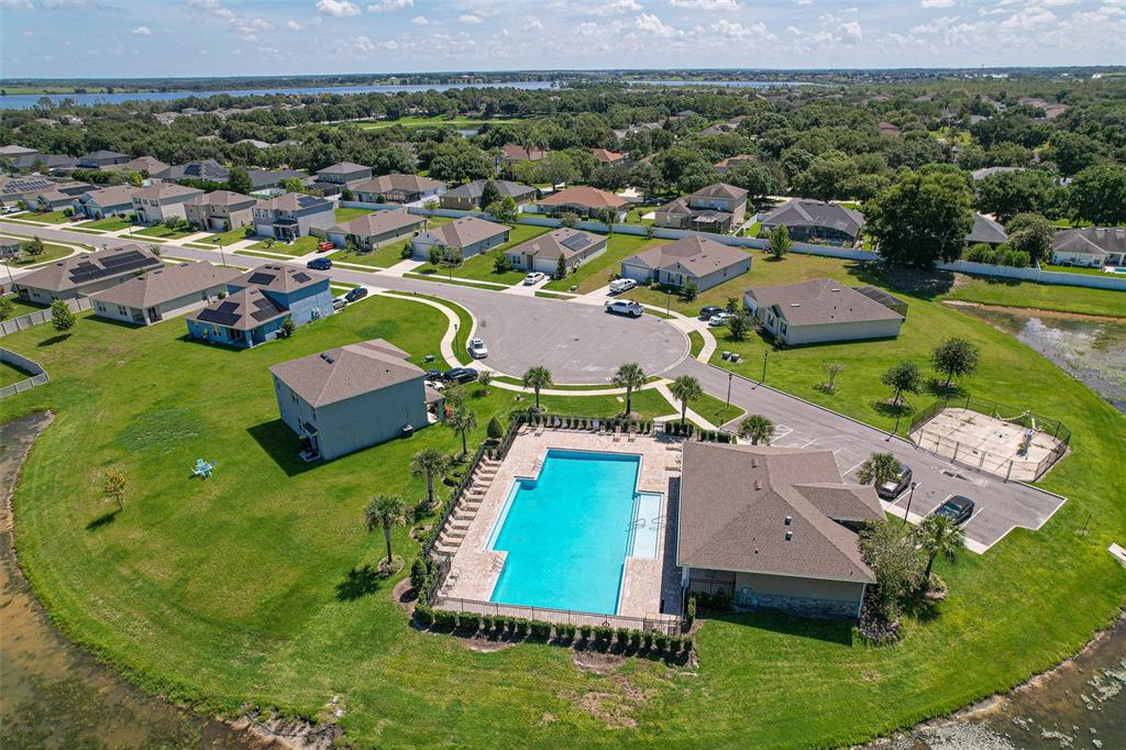 An aerial view shows a community swimming pool, clubhouse, and surrounding residential homes near water — 759 AUBURN GROVE COURT, AUBURNDALE, FL