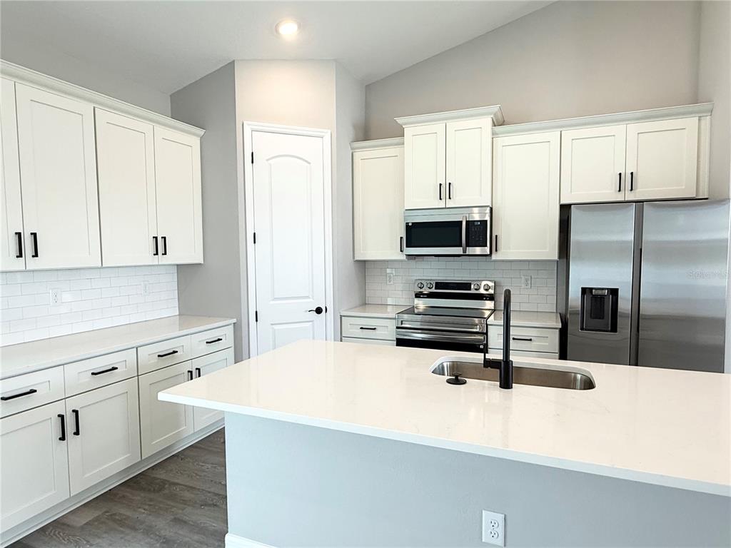 A modern kitchen features white cabinets, stainless steel appliances, a quartz island, and subway tile — 4645 BOSTON STREET, SEBRING, FL