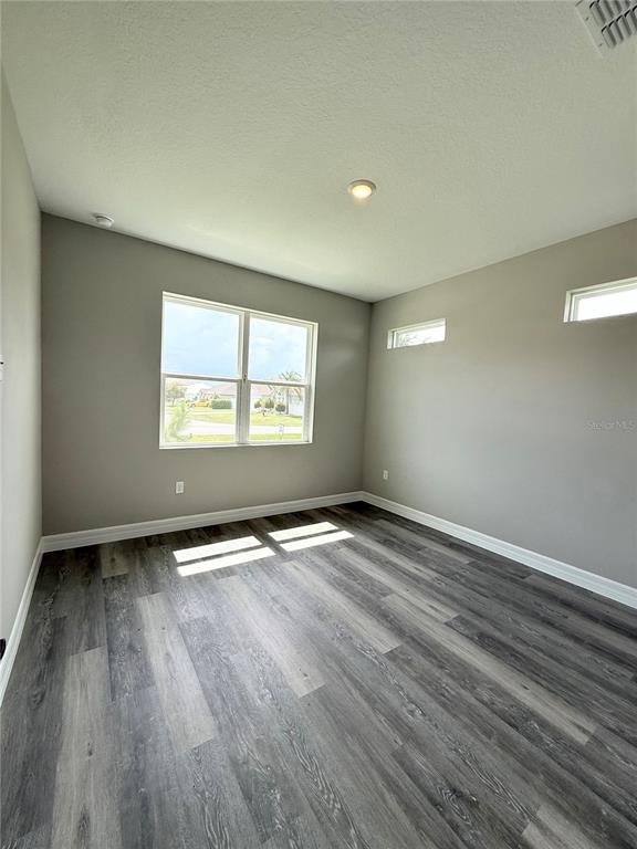An empty room with gray walls, wood-look flooring, a large window, and two clerestory windows — 4645 BOSTON STREET, SEBRING, FL